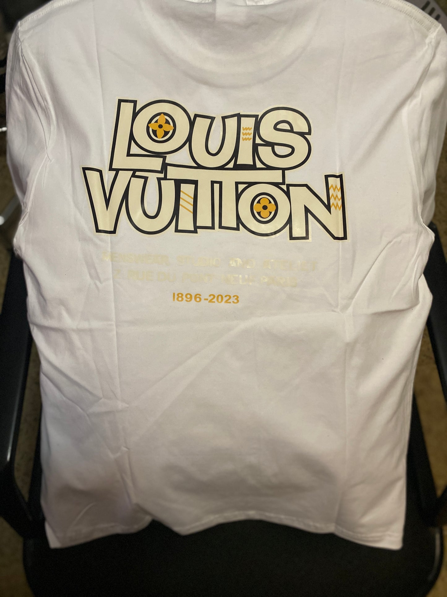 White sleeveless shirt with 'Louis Vuitton' logo and text on a chair.